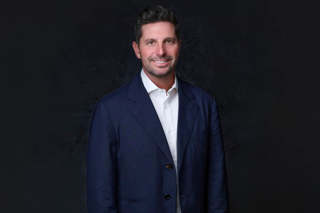 Mac Cummings standing in a navy suit smiling into camera
